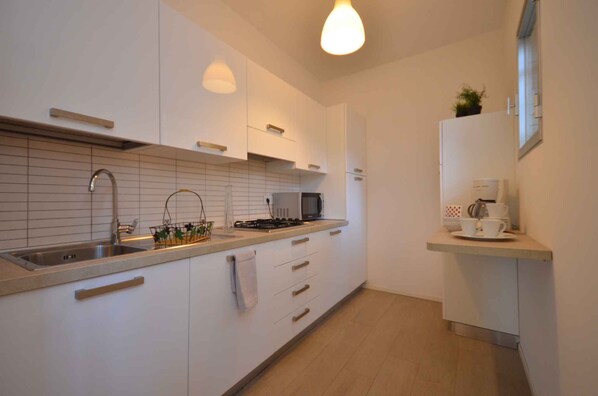 A modern kitchen with white cabinets, a stainless steel sink, a microwave, and a small countertop with a coffee maker.