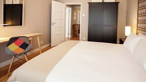 A hotel room with a bed, a desk, a chair, a wardrobe, and a door leading to another room. - "House of Joy" Apartment (Porto)