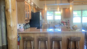 Una cocina rústica con vigas de madera, una isla grande con taburetes y una mesa de madera con detalle de cuero.