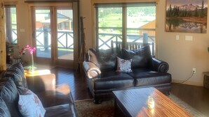 Amplia sala de estar con sofás de cuero, una mesa de centro de madera y grandes ventanales con vistas al exterior.