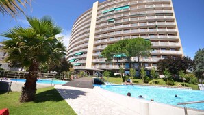 A multi-story hotel with a swimming pool, palm trees, and a clear blue sky.