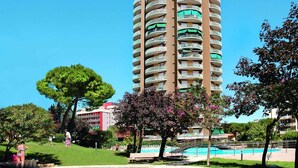 A tall, multi-story hotel with balconies, surrounded by greenery and a swimming pool.