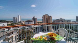 A balcony with a table set for two, overlooking a cityscape with buildings and a beach.