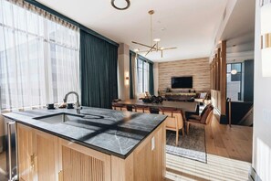 A modern kitchen with a central island, a dining area with wooden furniture, and a large TV mounted on the wall.
