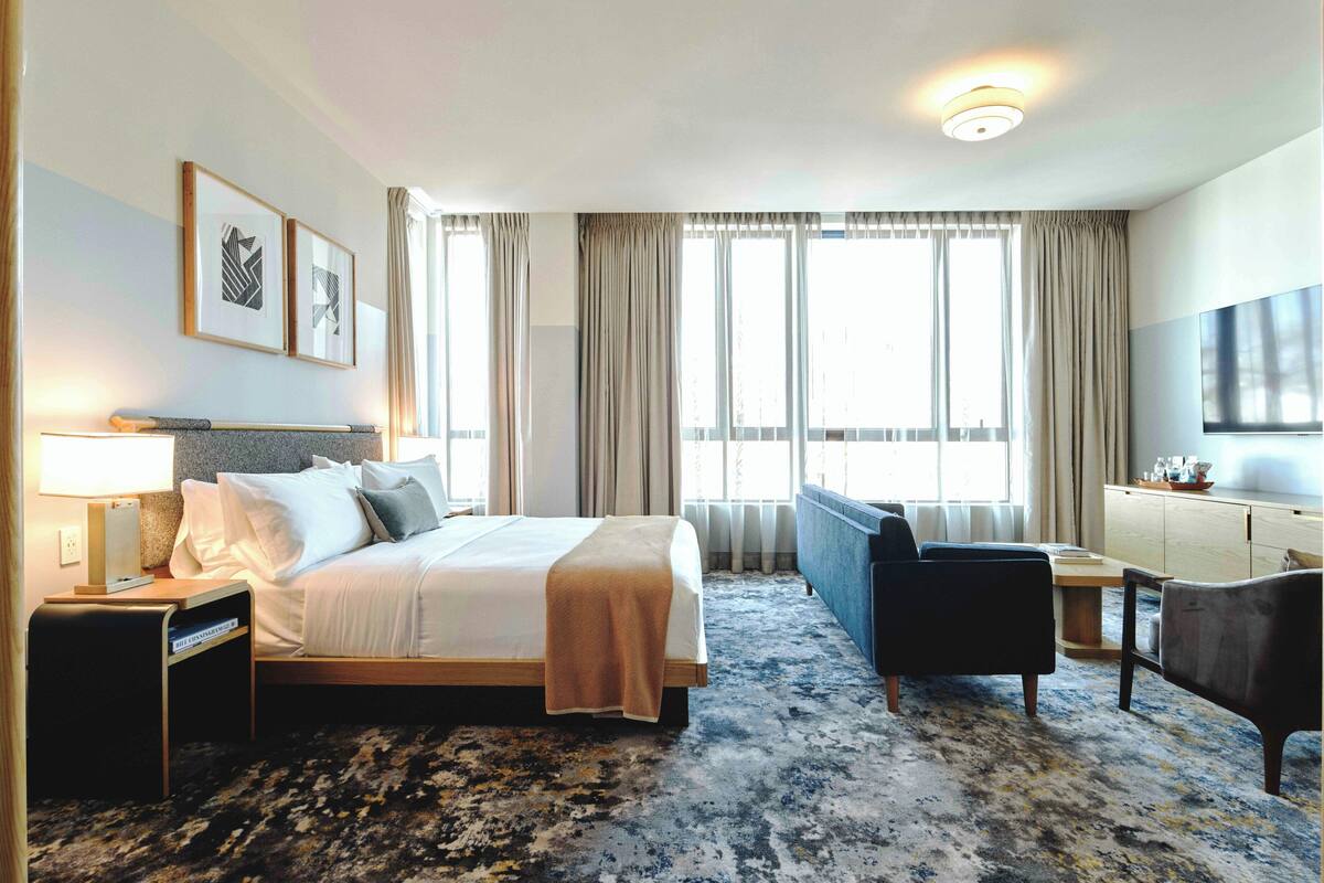 A hotel room with a bed, bedside table, lamp, and a sofa.