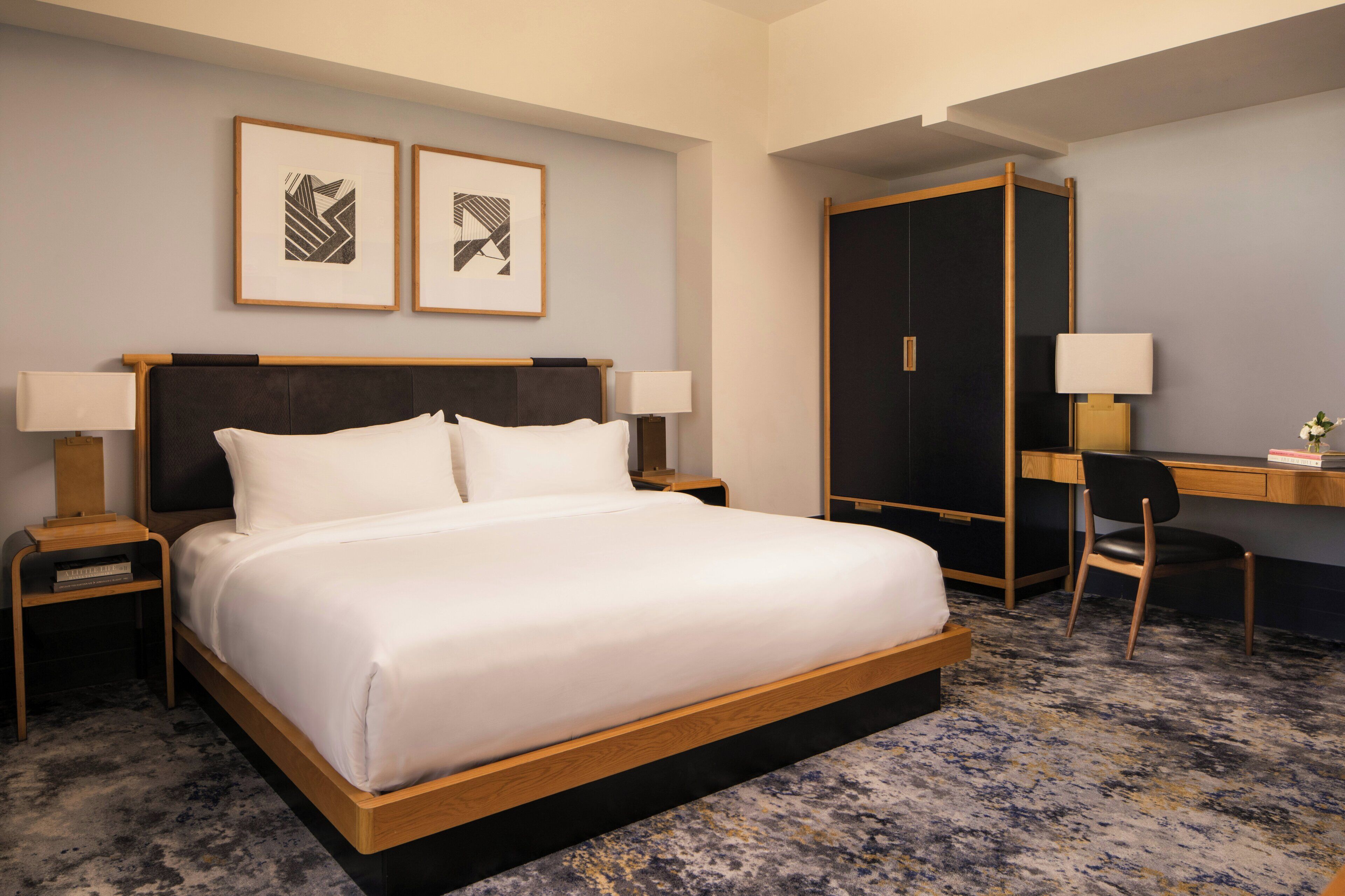 A hotel room with a bed, two bedside tables, a desk, a chair, and two framed pictures on the wall.
