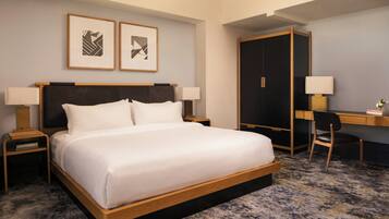 A hotel room with a bed, two bedside tables, a desk, a chair, and two framed pictures on the wall.