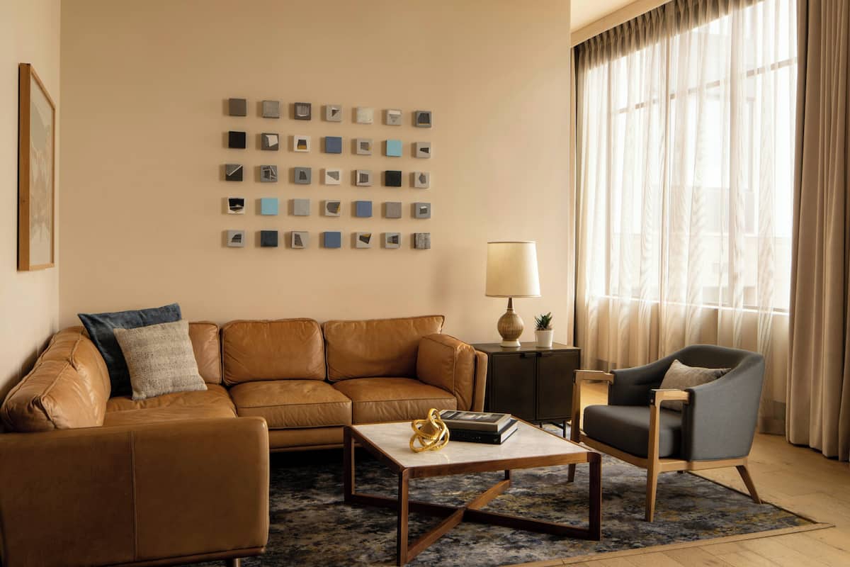 A living room with a brown leather sofa, a grey armchair, a coffee table, a lamp, and a wall of framed pictures.