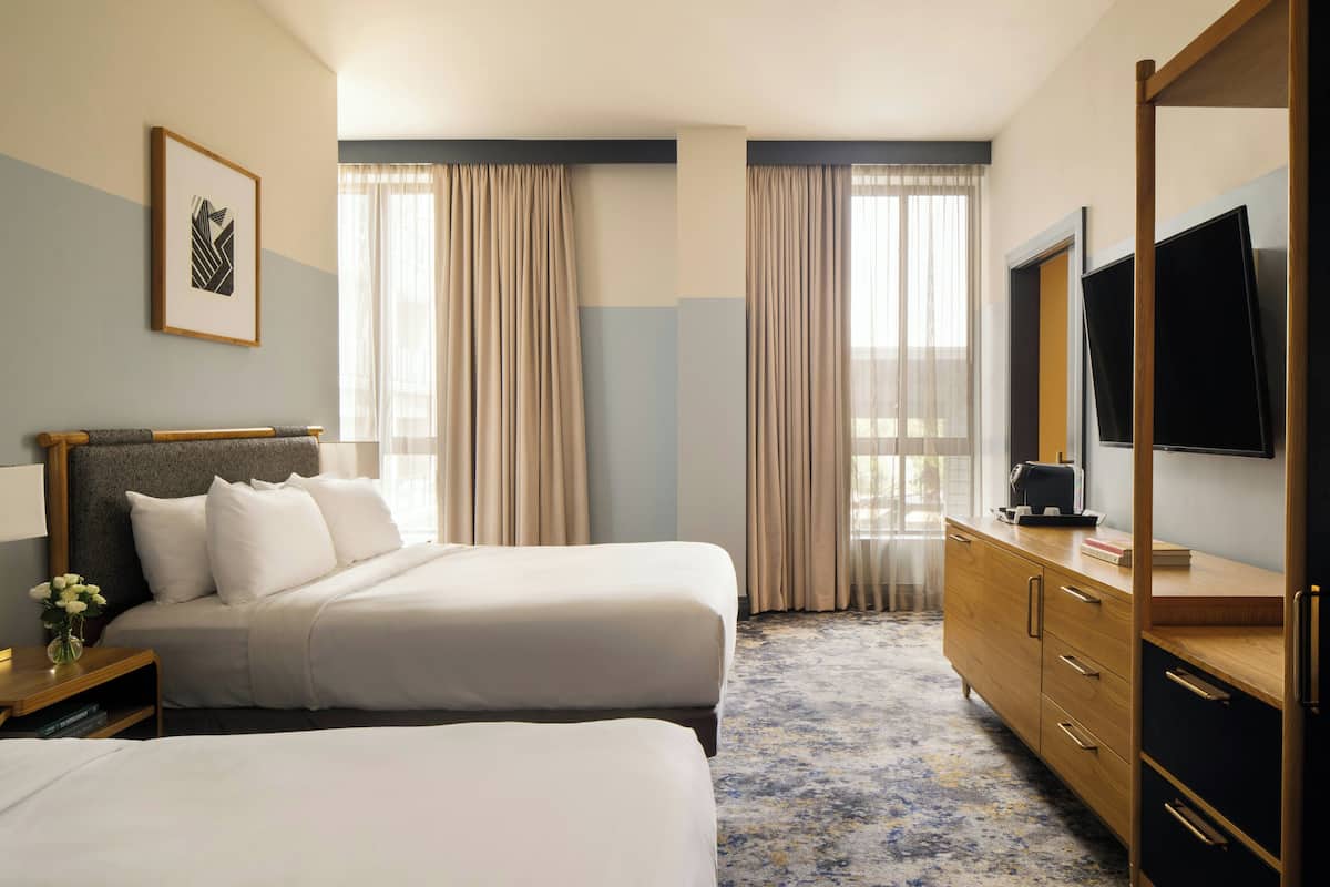 A hotel room with two beds, a wooden dresser, a flat-screen TV, and a framed picture on the wall.