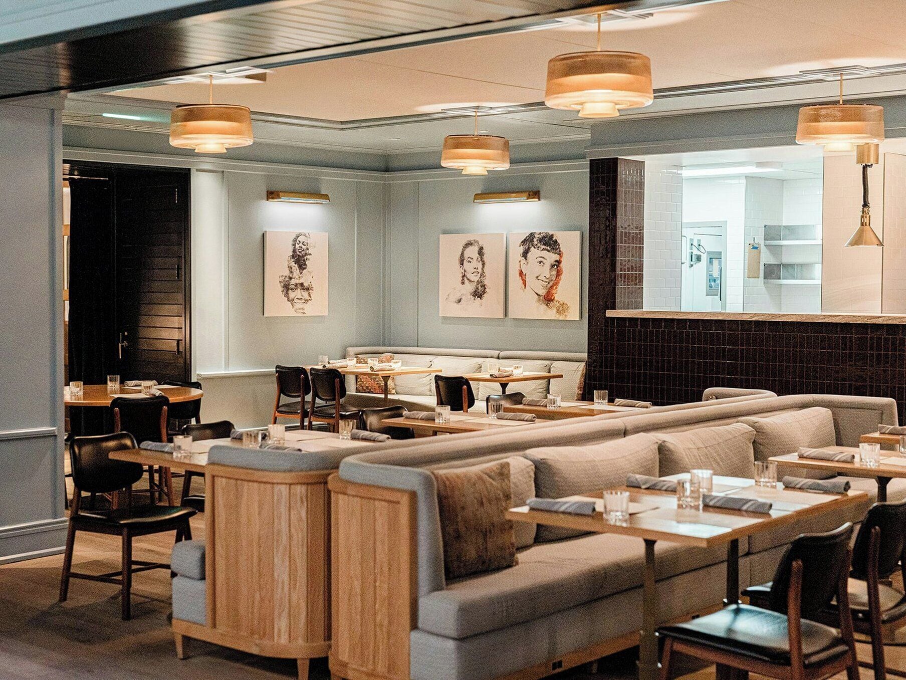 A restaurant with a long counter, cushioned seating, pendant lighting, and artwork on the walls.
