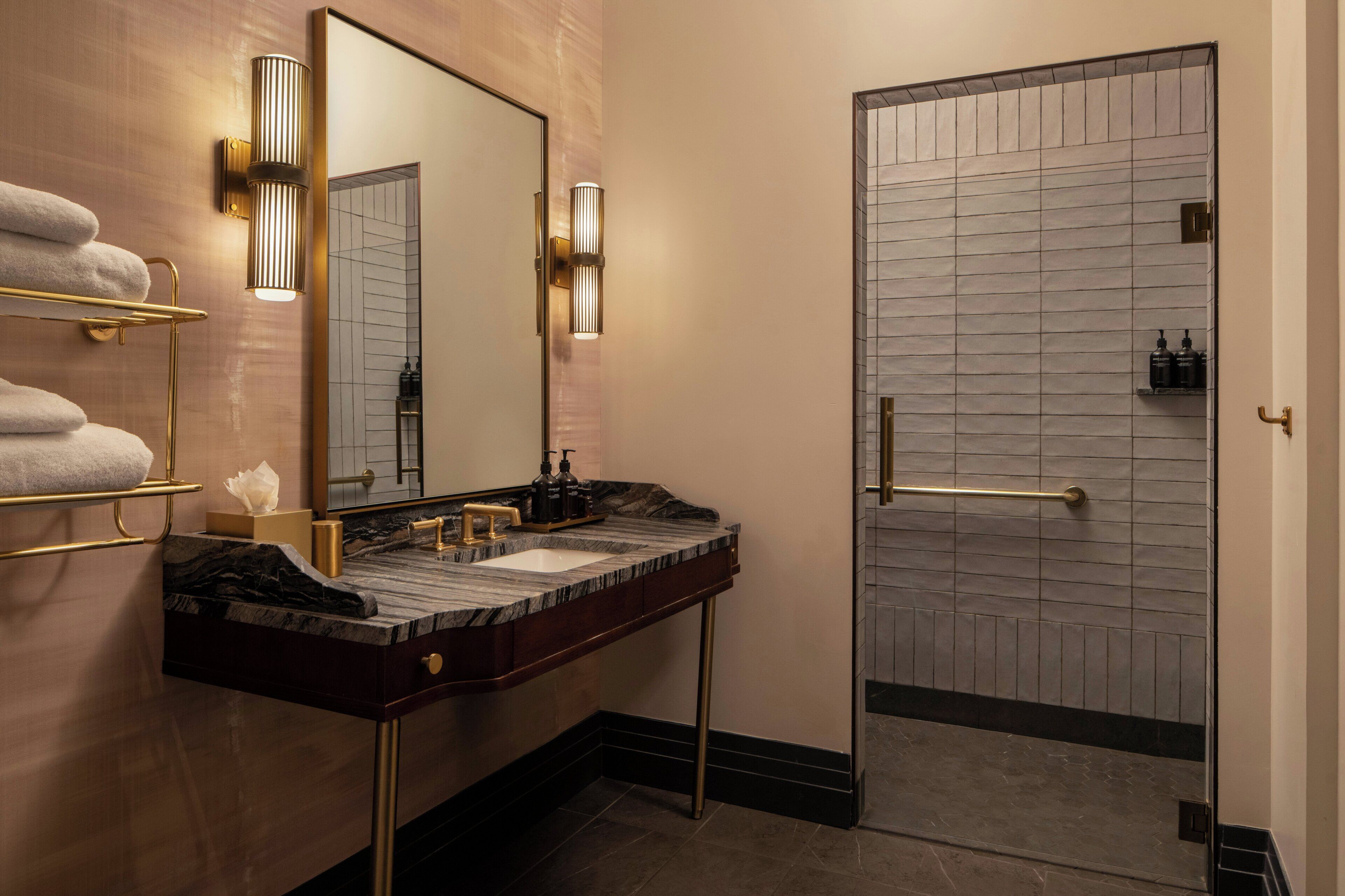 A modern bathroom with a marble sink, gold fixtures, and a glass shower enclosure.