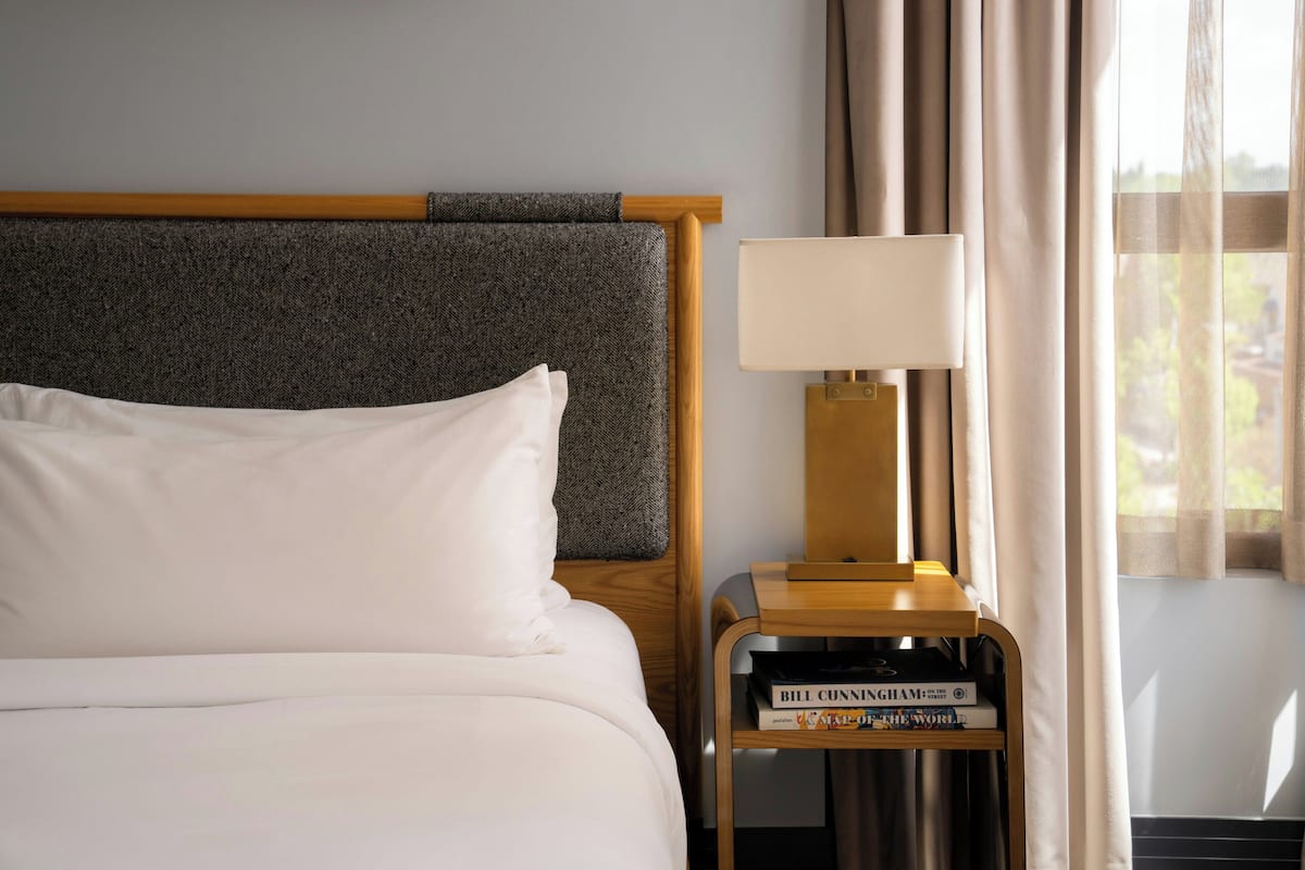 A hotel room with a bed, a nightstand with a lamp, and a window with curtains.