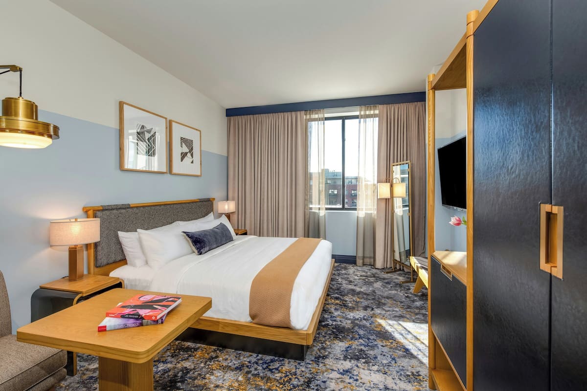A hotel room with a bed, bedside tables, a TV, a desk, and a window with curtains.