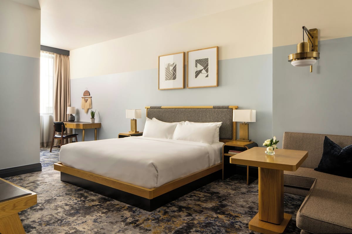A hotel room with a bed, bedside tables, a sofa, a desk, and a chair.