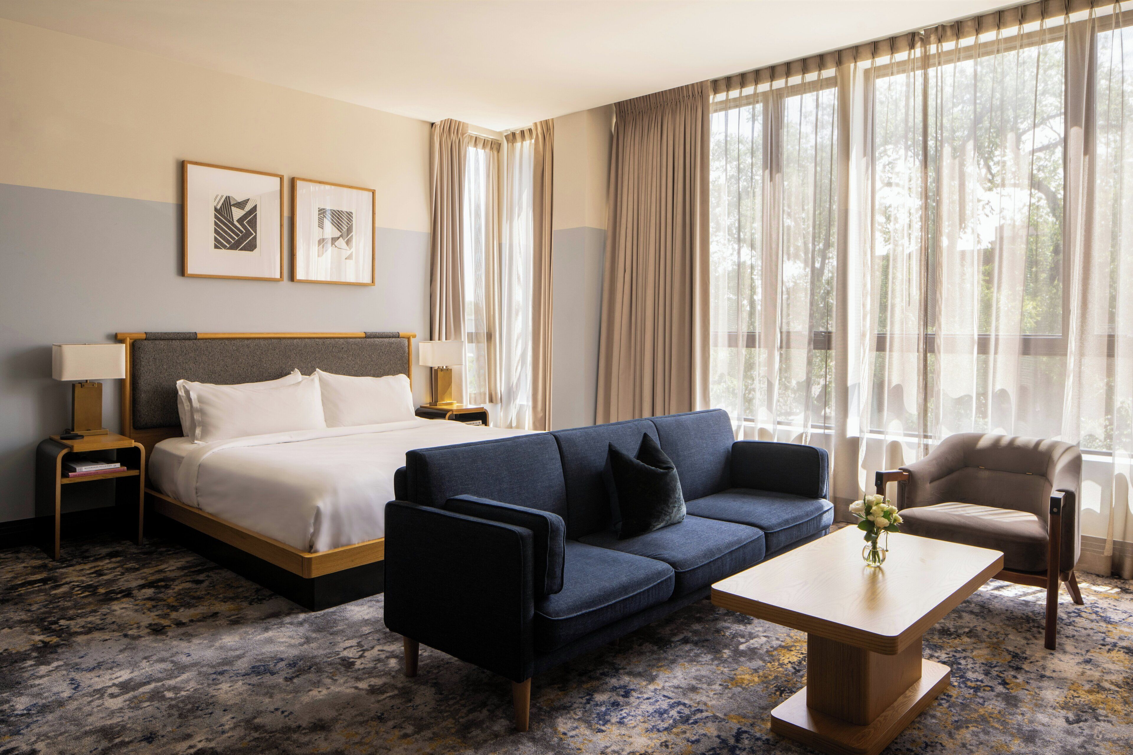 A hotel room with a bed, a sofa, a chair, a nightstand, a lamp, and a window with curtains.