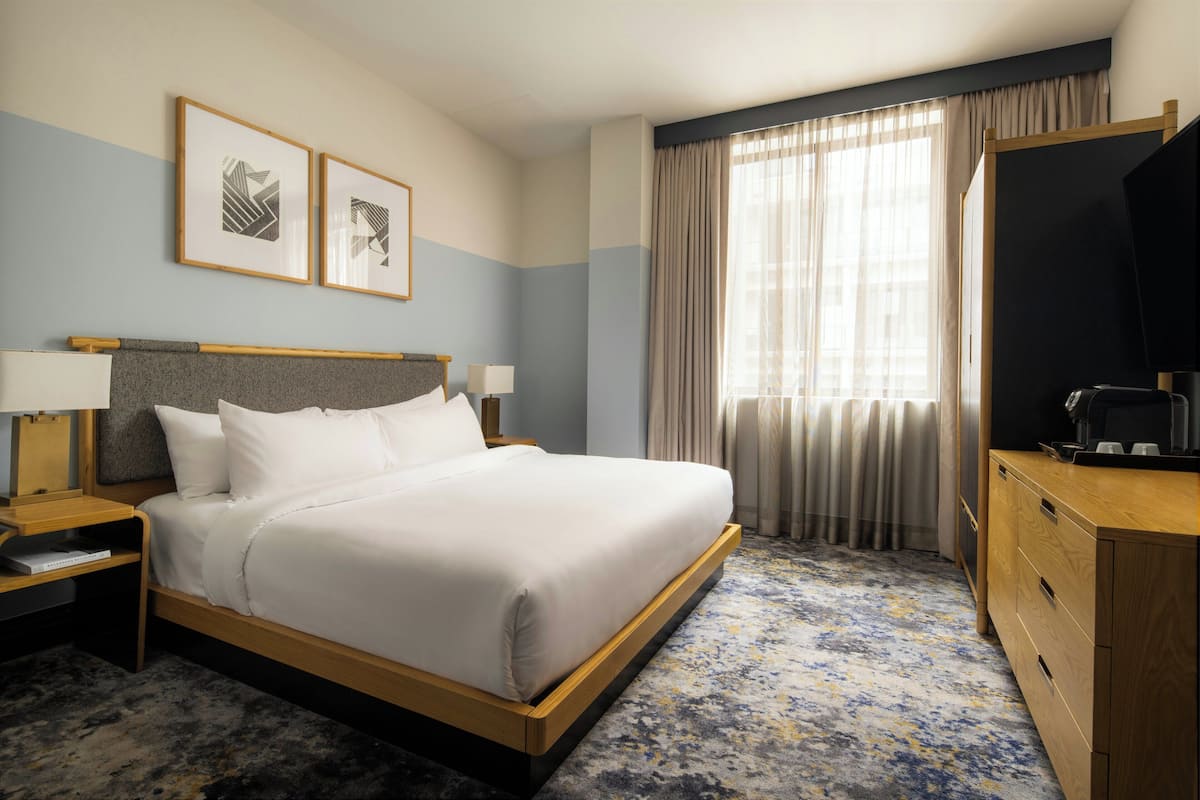 A hotel room with a bed, bedside tables, a TV, a dresser, and curtains.