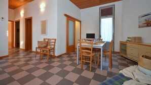Una habitación con suelo a cuadros, techo de madera, una mesa de comedor con sillas, un televisor y una ventana con persianas.