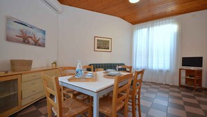 Un comedor con mesa y sillas de madera, mostrador de buffet, televisor y un cuadro de un barco en la pared.