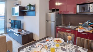 Una cocina moderna con armarios rojos, un microondas y un refrigerador. Se observa una mesa de comedor con alimentos para el desayuno y un televisor al fondo.