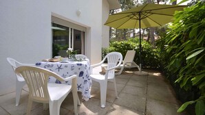 An outdoor patio with a table set for two, white plastic chairs, and a yellow umbrella. - Holiday apartment with air conditioning (Lignano)