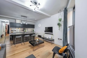 A modern kitchen with a central island, bar stools, a dining table, and a TV mounted on the wall.