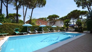 Una piscina con sillones de descanso y sombrillas, rodeada de árboles y edificios.