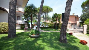 Una zona residencial con césped cuidado, varios árboles y un acceso con portón.