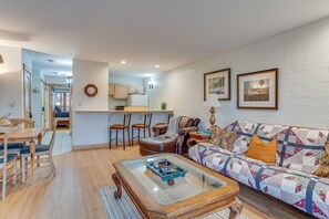 A cozy living room with a wooden coffee table, a sofa with a quilt, and a kitchen in the background. - ⭐️ Mtn Village ⭐️ Private Deck ⎮ HotTub ⎮ Free WIFI + Fireplace (Steamboat Springs)