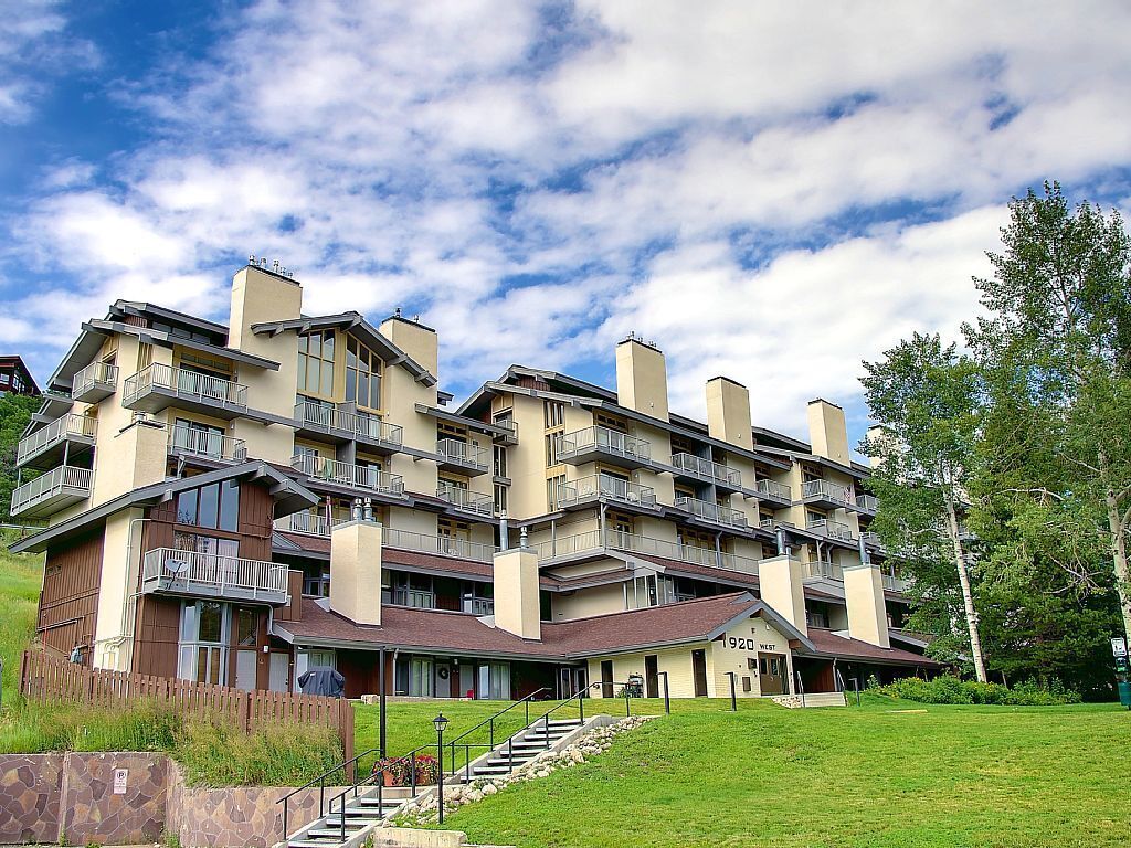 Un hotel de varios pisos con balcones, fachada de piedra y un césped.