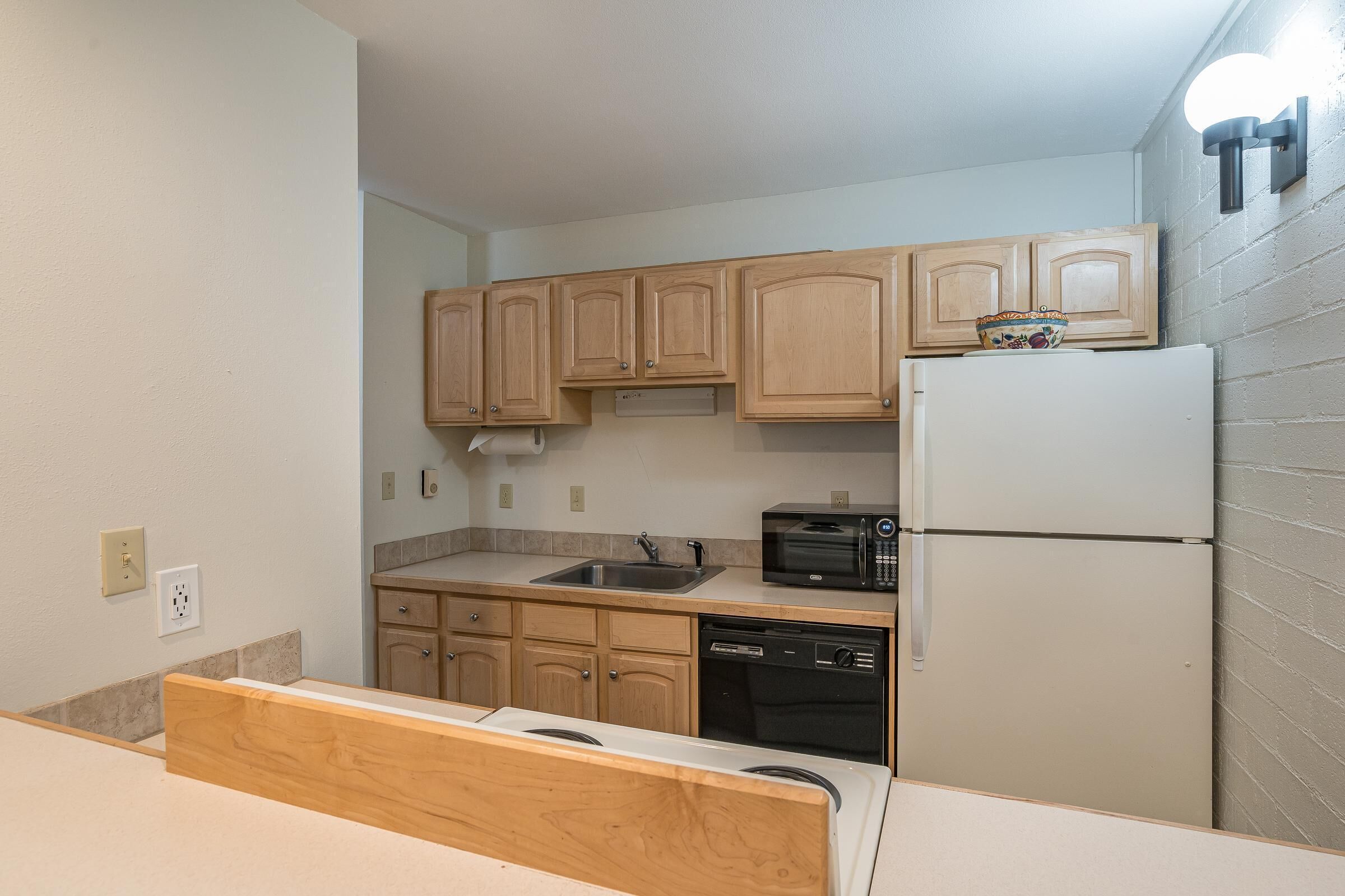 Una cocina compacta con armarios de madera, un refrigerador blanco, un microondas y un lavavajillas.