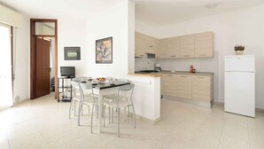 A modern kitchen with white cabinets, a white refrigerator, and a dining area with a table and chairs. - Holiday apartment with air conditioning and pool (Lignano)