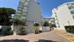 A modern building with multiple balconies, a paved entrance area, and surrounding greenery. - Holiday apartment with air conditioning and pool (Lignano)