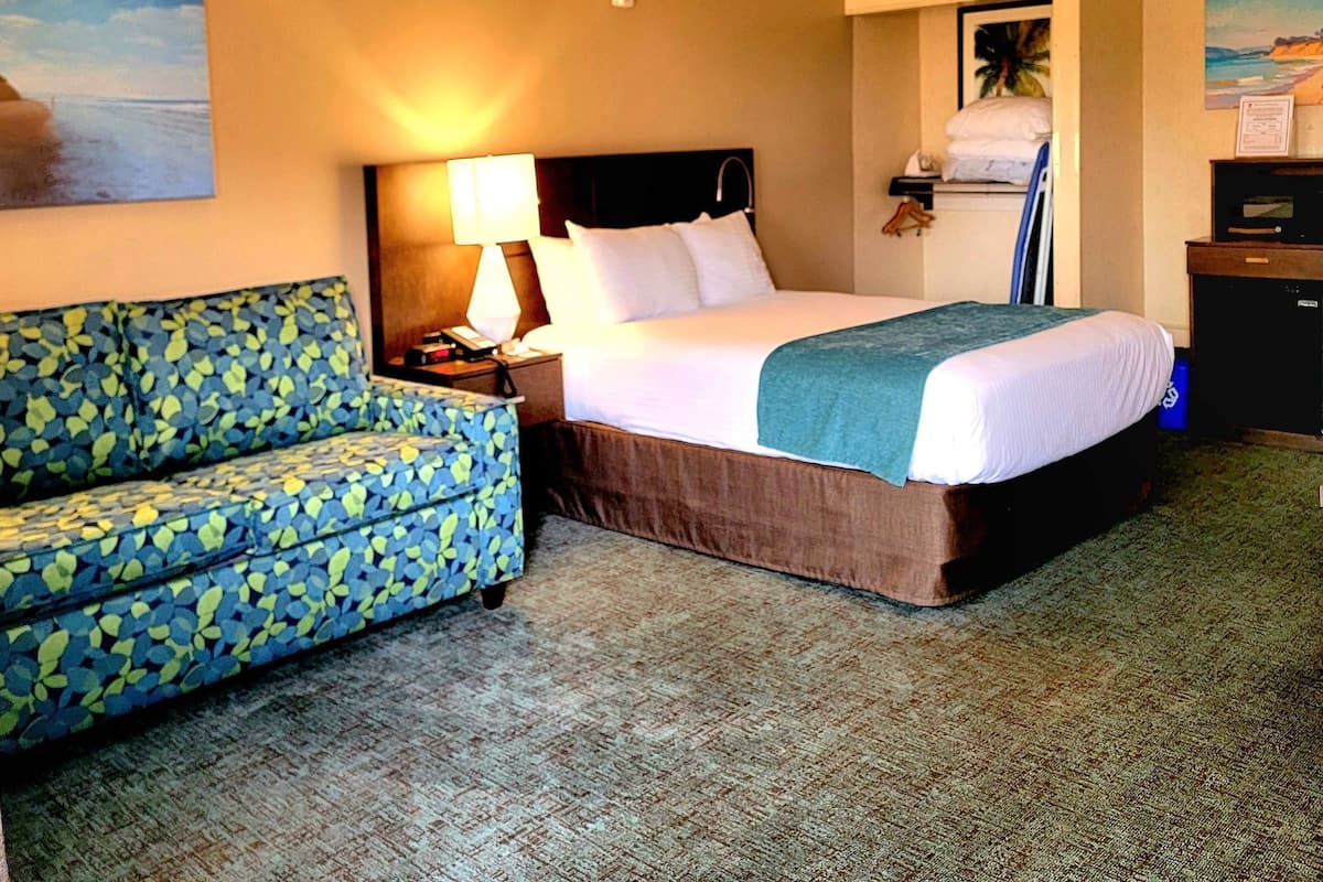 A hotel room with a bed, a sofa, a lamp, and a painting on the wall.