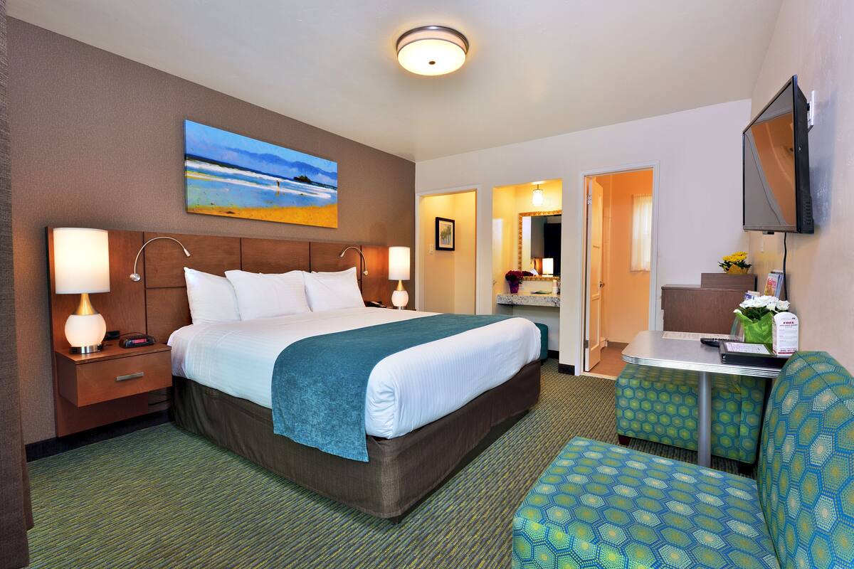 A hotel room with a bed, bedside table, lamp, and a painting on the wall.