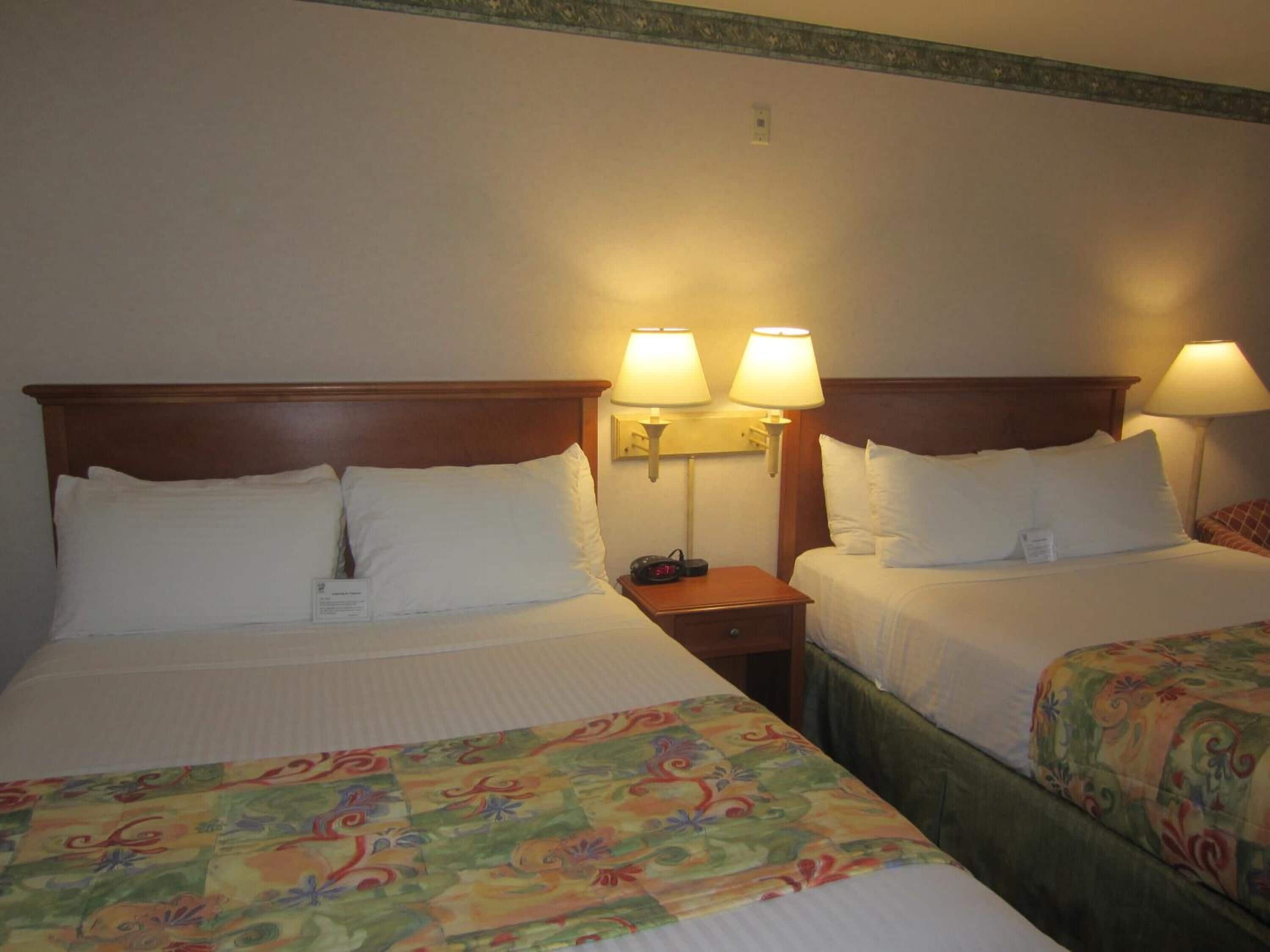 Een hotelkamer met twee bedden, elk voorzien van een houten hoofdbord en witte beddengoed. Op elk bed staan twee bedlampen.
