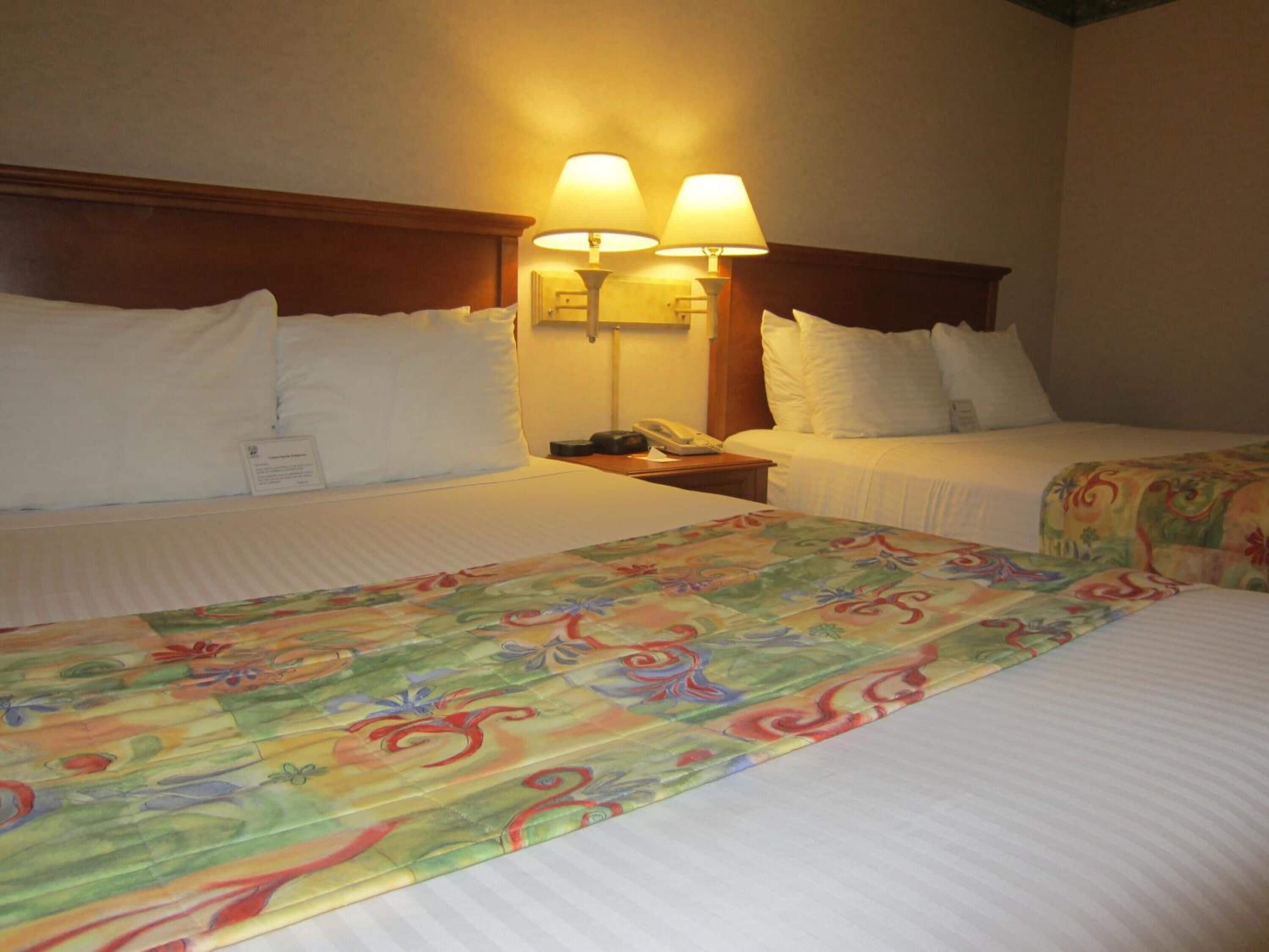 A hotel room with two beds, each with white linens and a wooden headboard. There are two bedside lamps on the nightstands.
