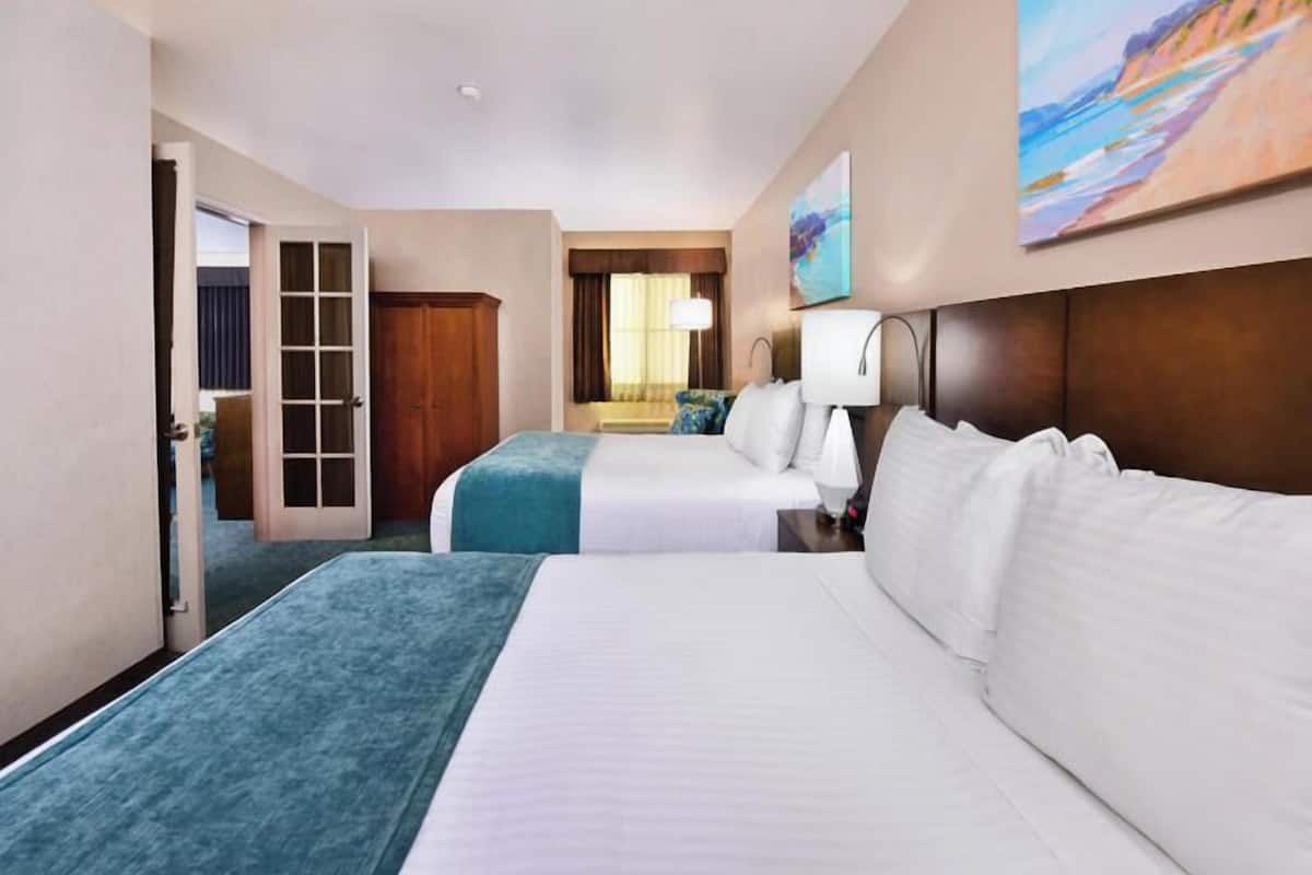 A hotel room with two beds, a large window, a painting on the wall, and a door leading to another room.
