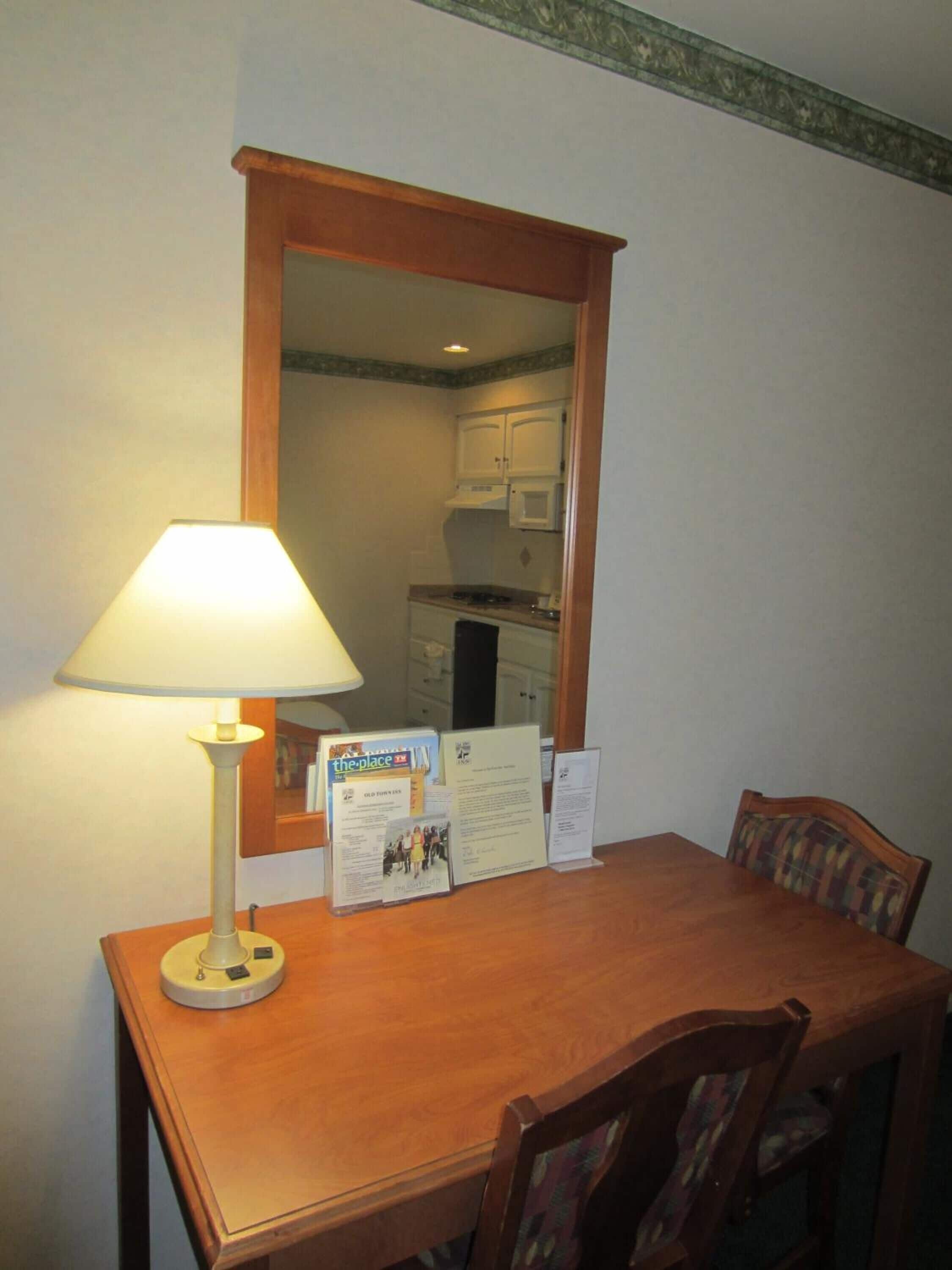 A wooden dining table with a lamp, chairs, and informational brochures.