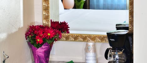 Un baño de hotel con espejo, un jarrón de flores, una cafetera y un dispensador de toallas.