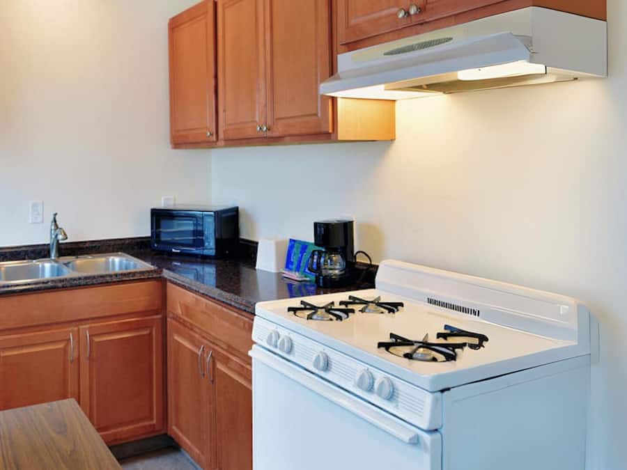 A compact kitchen with wooden cabinets, a gas stove, a microwave, and a sink.