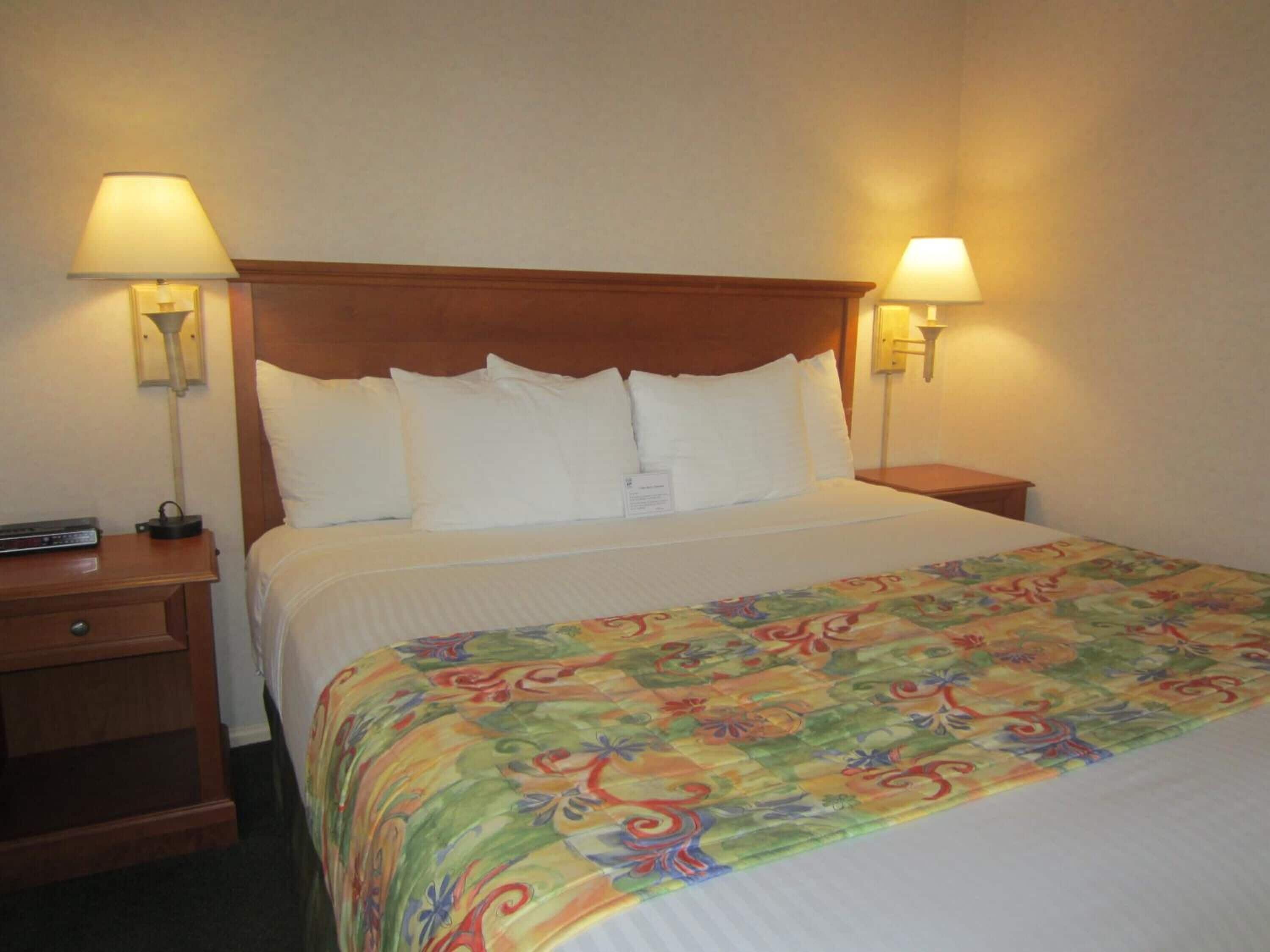 A hotel room with a wooden headboard, white bedding, and two bedside lamps.