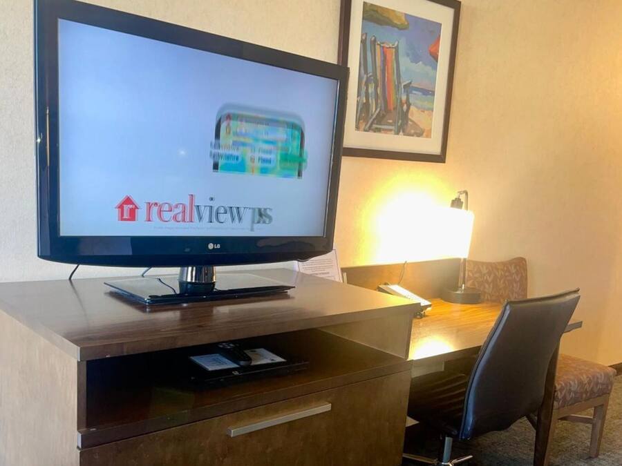 Une chambre d’hôtel équipée d’un grand téléviseur à écran plat affichant « realview ps » à l’écran, d’un bureau avec une lampe, d’une chaise et d’une petite commode à tiroirs.