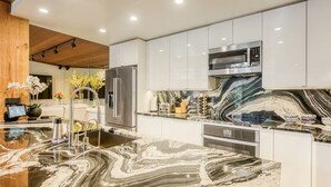 A modern kitchen with a marble countertop, stainless steel appliances, and white cabinetry. - Lake Tahoe’s Ultimate Family & Friends Retreat (Olympic Valley)