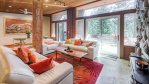 A spacious living room with a large window, a stone wall, and a ceiling fan. - Lake Tahoe’s Ultimate Family & Friends Retreat (Olympic Valley)