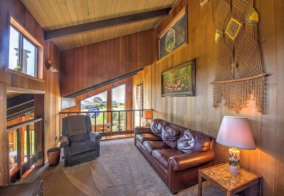 A spacious living area with a leather sofa, a chair, a lamp, and a view through large windows.