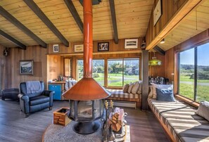 A cozy interior with a large fireplace, seating areas, and large windows offering a view of the outdoors.