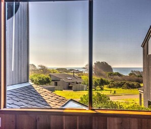 A view through a window of a residential area with houses, a grassy yard, and a body of water in the distance. - Quail View - Spacious Sea Ranch Family Lodge (Sea Ranch)