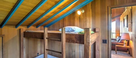 A bunk bed room with a wooden ceiling and a visible door leading to another room.