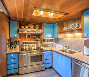 A modern kitchen with stainless steel appliances, blue cabinetry, and a granite countertop.