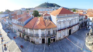 Un edificio histórico con techo de tejas, una estatua y vista a una colina con una iglesia.